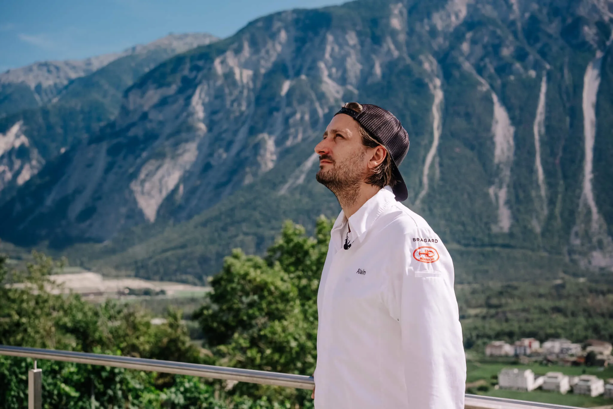 Alain Lerjen in profile in a white chef’s jacket, the rock face behind him